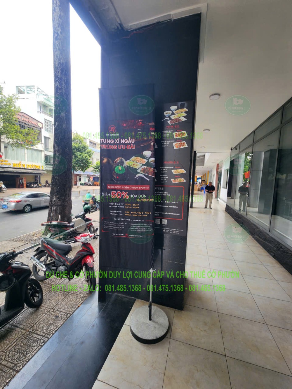 Cờ chữ nhật màu đen với nội dung “Tung xí ngầu trúng ưu đãi”, đặt dưới mái hành lang trước nhà hàng.