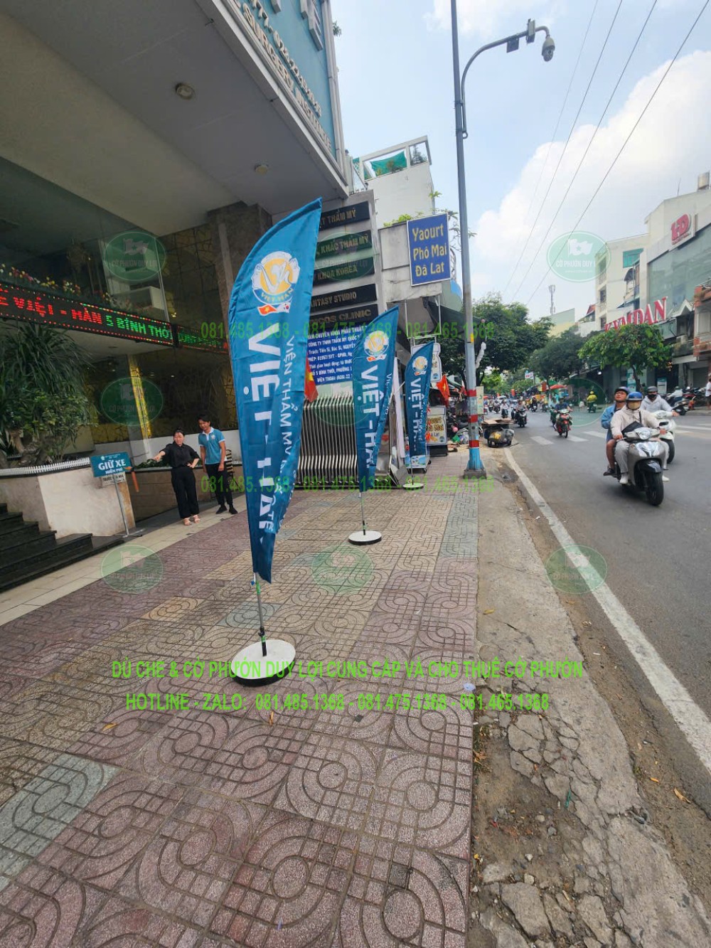 Dãy cờ nền xanh mang nội dung viện thẩm mỹ được bố trí dọc mặt tiền, lặp lại nhận diện thương hiệu.
