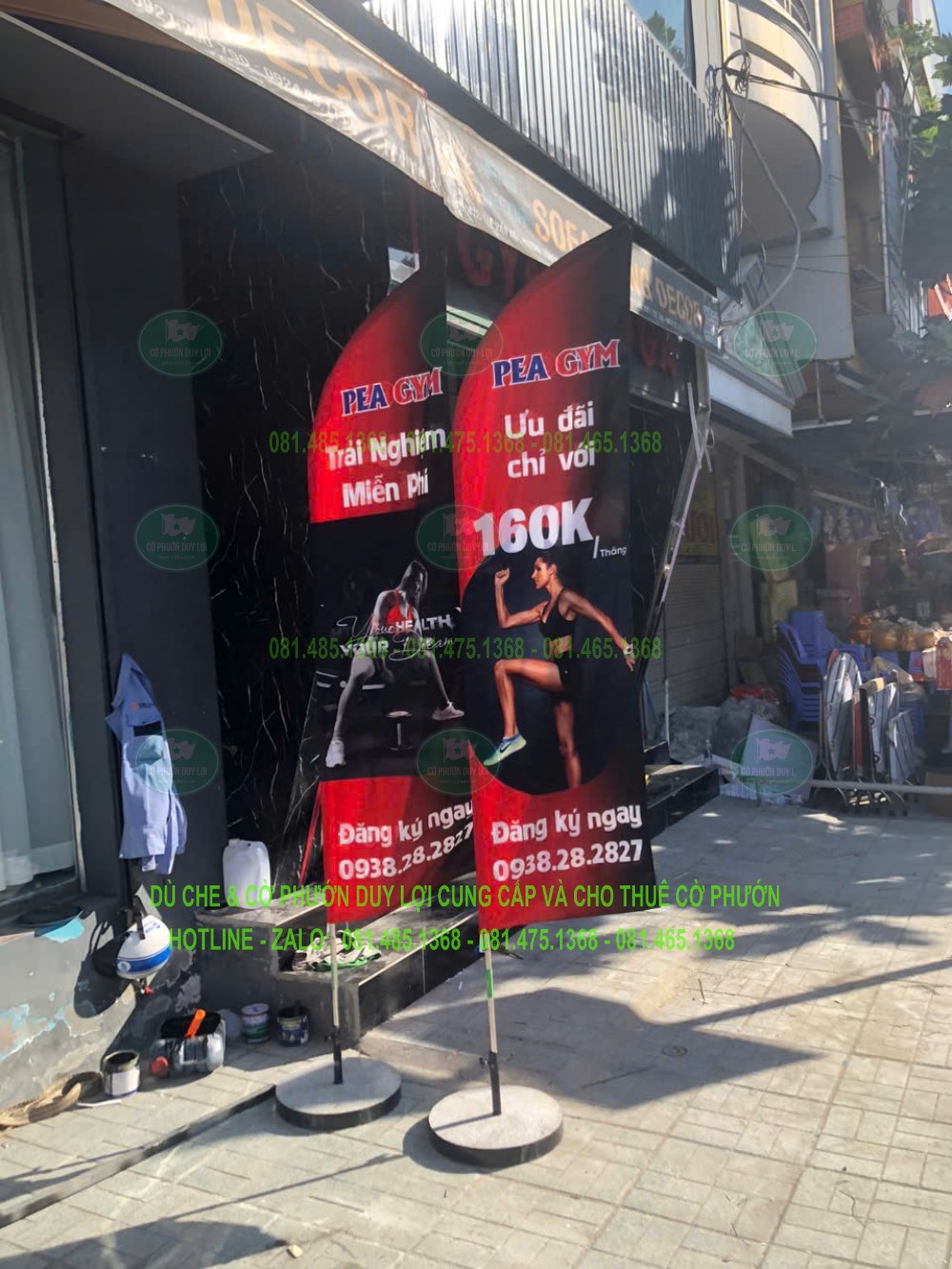 Hai cờ quảng cáo mang nội dung khác nhau được dựng trước mặt tiền bằng các đế rời.