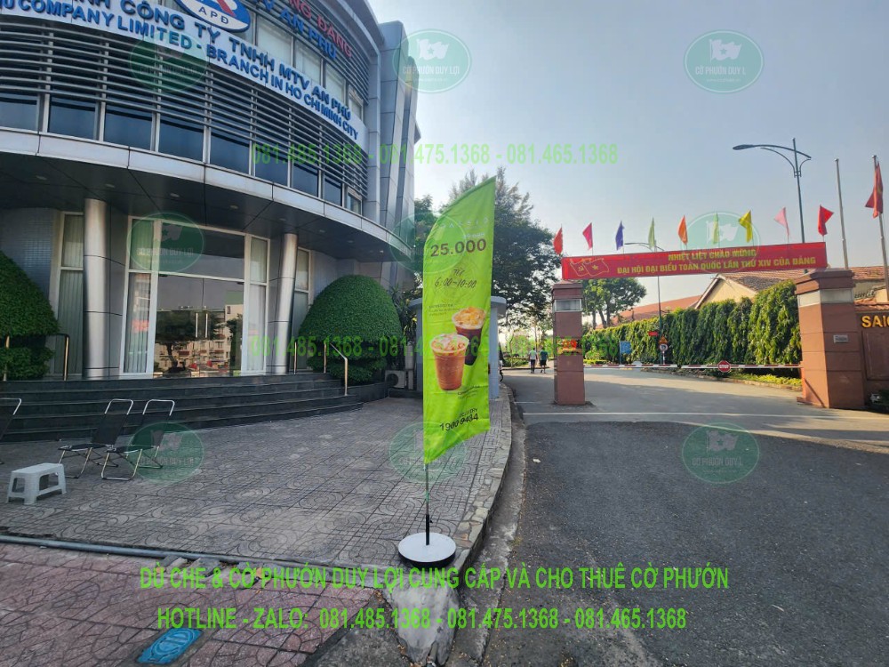 Cờ phướn cánh buồm nền xanh in hình đồ uống, đặt cạnh khu vực lối vào và khoảng sân phía trước tòa nhà.