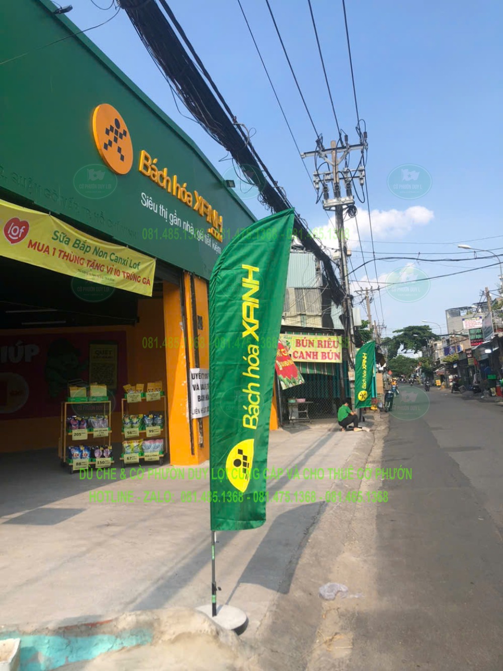 Cờ Bách Hóa Xanh đặt phía trước siêu thị, với tên thương hiệu màu vàng hiển thị theo chiều dọc.