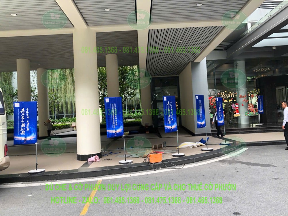 Nhiều cờ chữ nhật nền xanh được dựng dọc khu vực sảnh, theo một quy cách nhận diện thống nhất.