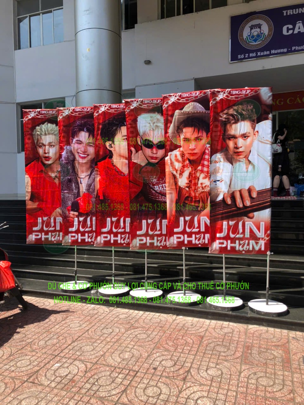Hàng cờ nền đỏ in hình và tên Jun Phạm, đặt trước khu vực bậc lên xuống của địa điểm tổ chức.