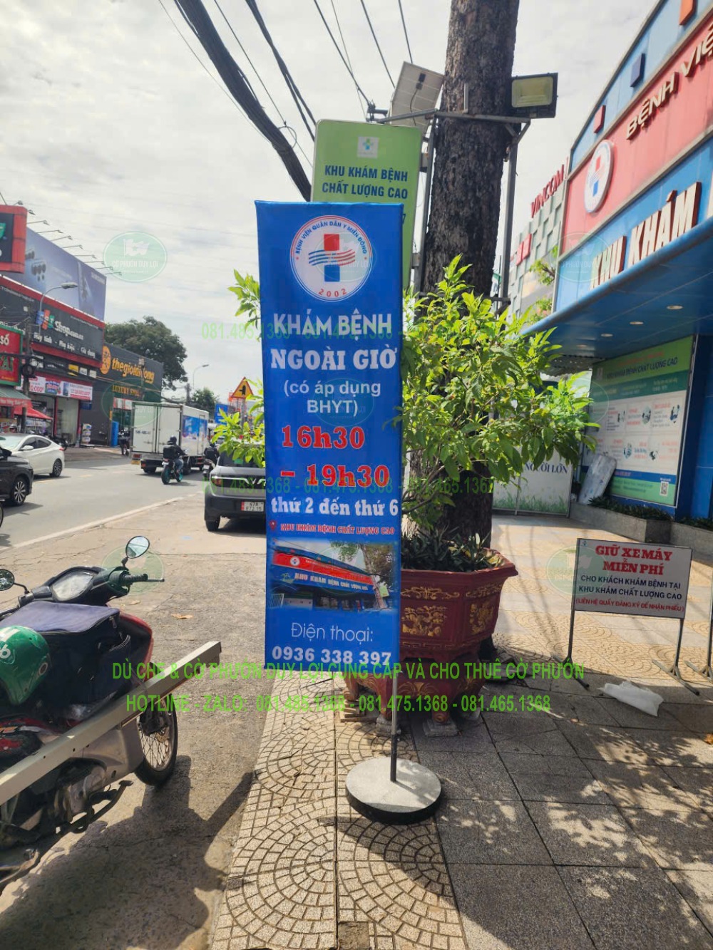Cờ chữ nhật màu xanh có dòng chữ “Khám bệnh ngoài giờ” được dựng trước mặt tiền phòng khám.