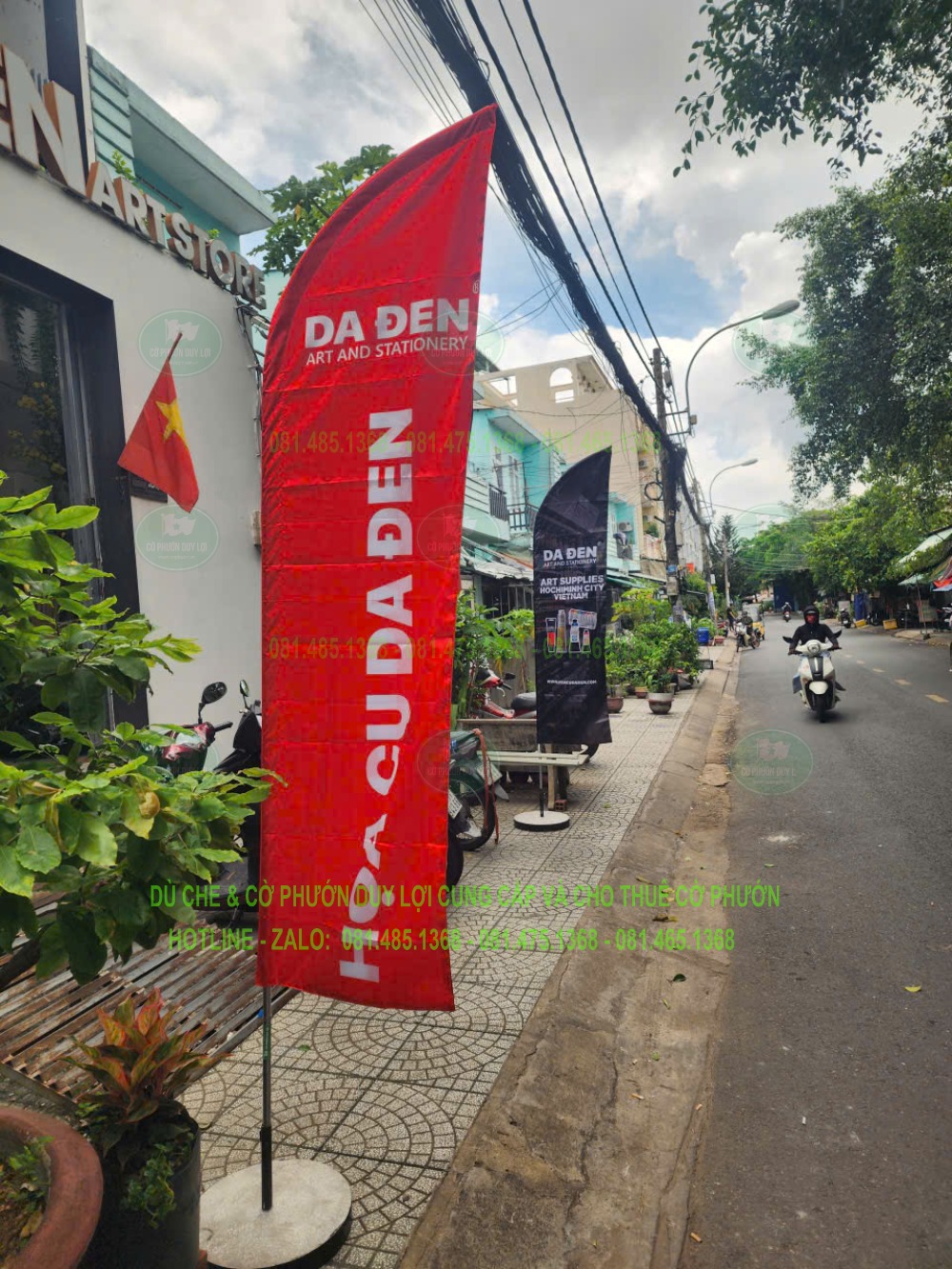 Cờ đỏ quảng cáo cửa hàng cầu lông được dựng bằng đế tròn trên nền lát trước cửa hàng.