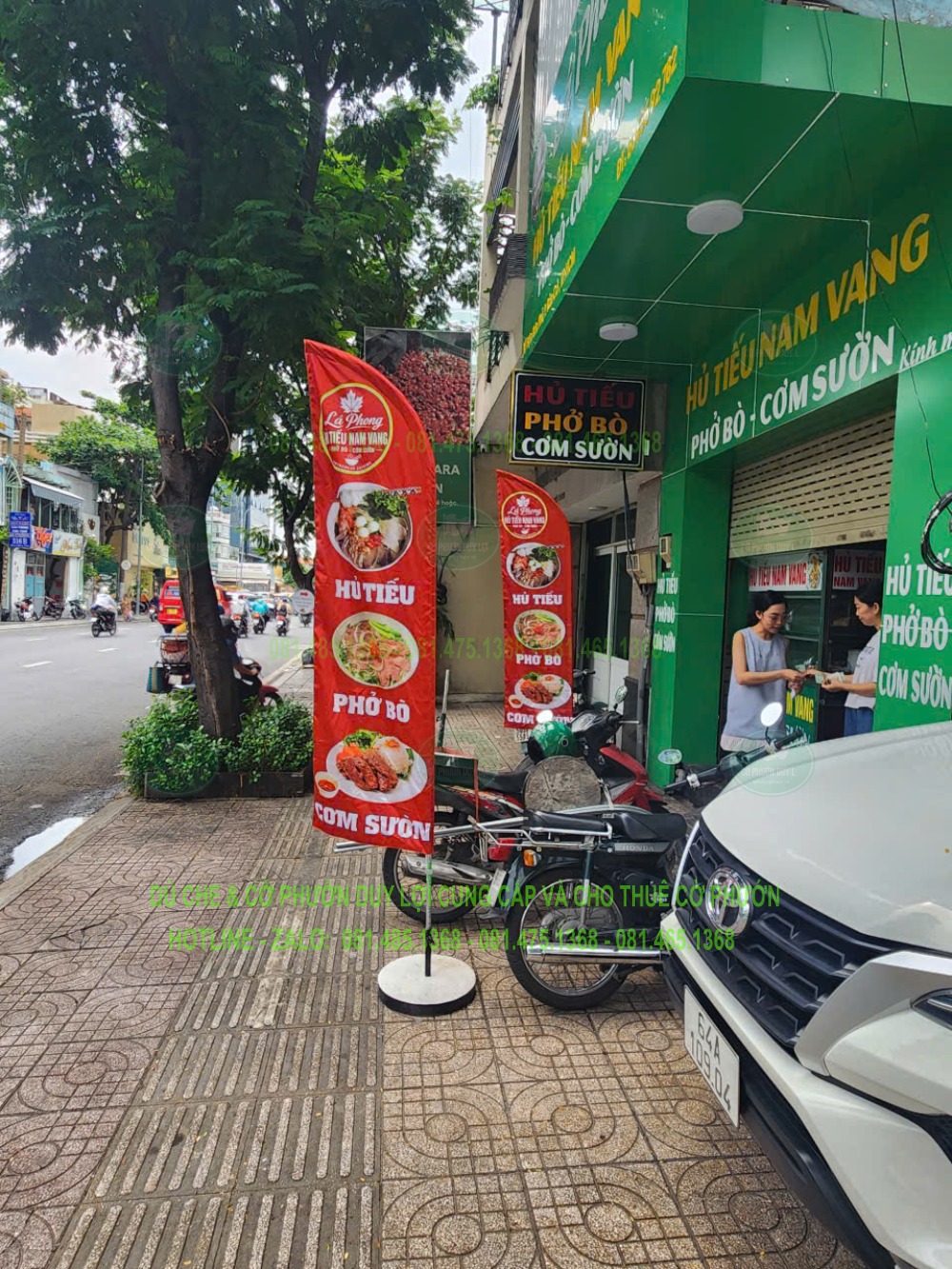 Cờ đỏ có hình món ăn và nội dung hủ tiếu, phở bò, cơm sườn được dựng cạnh mặt tiền quán.