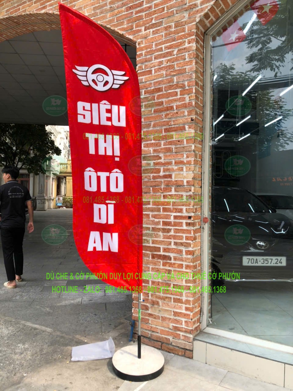 Cờ nền đỏ mang dòng chữ Siêu thị ô tô Dĩ An đặt cạnh lối vào showroom.