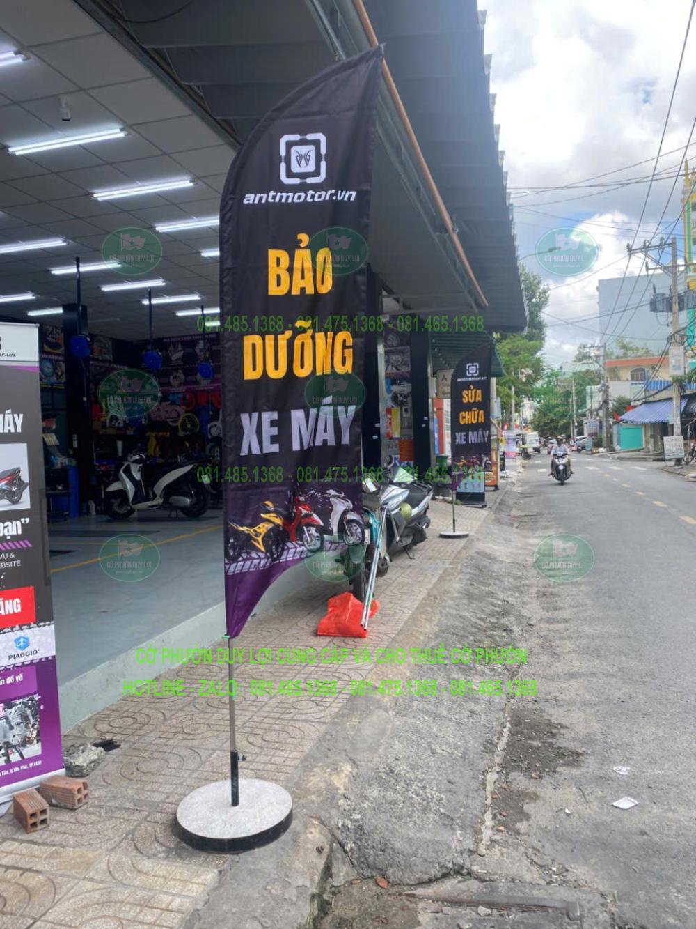 Cờ nền tối in chữ Bảo dưỡng xe máy bằng màu vàng và trắng, dựng trước cơ sở dịch vụ.