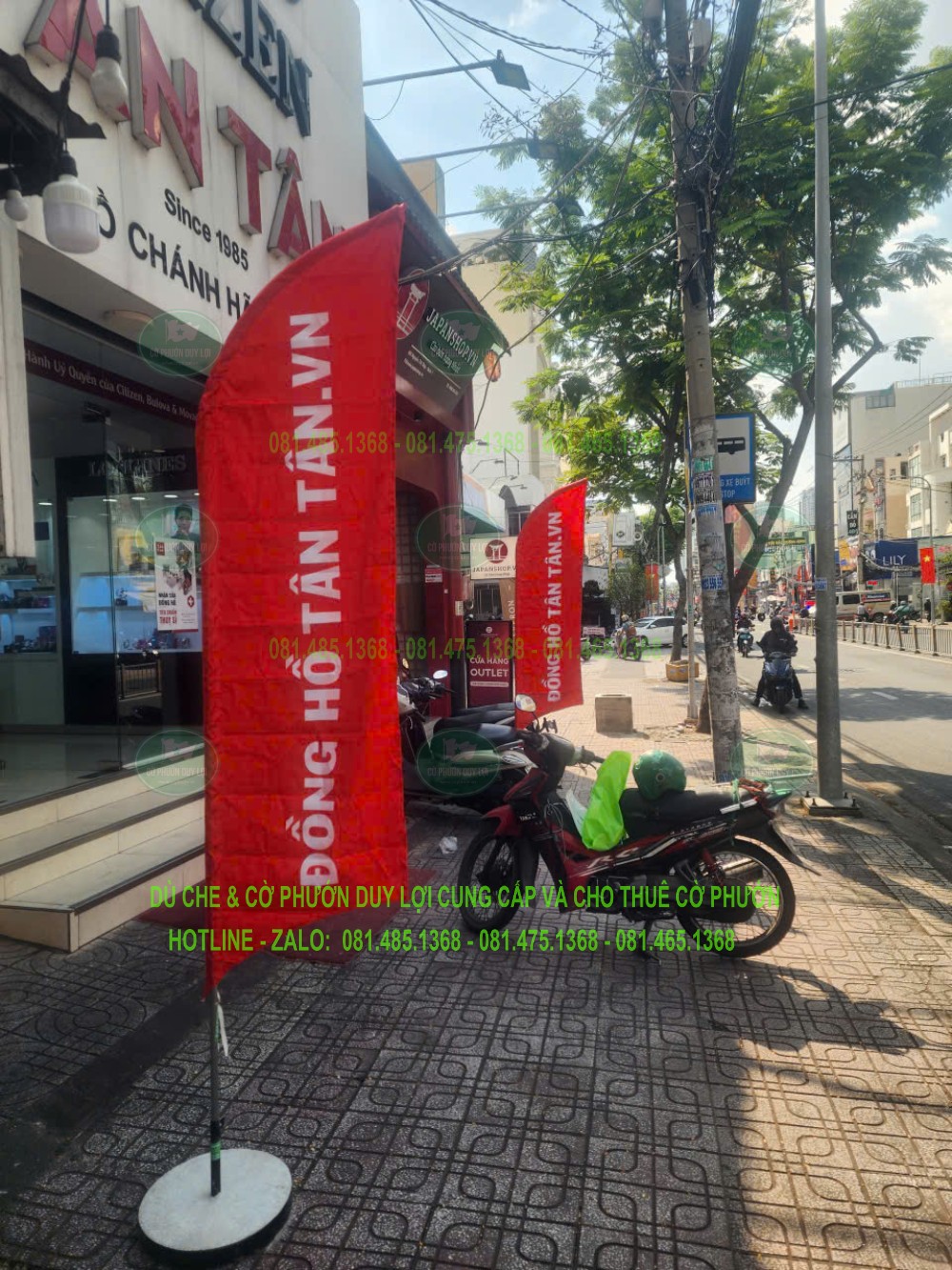 Cờ Đồng hồ Tân Tân nhìn gần, dựng bằng đế tròn cạnh khu vực mặt tiền và xe đỗ.