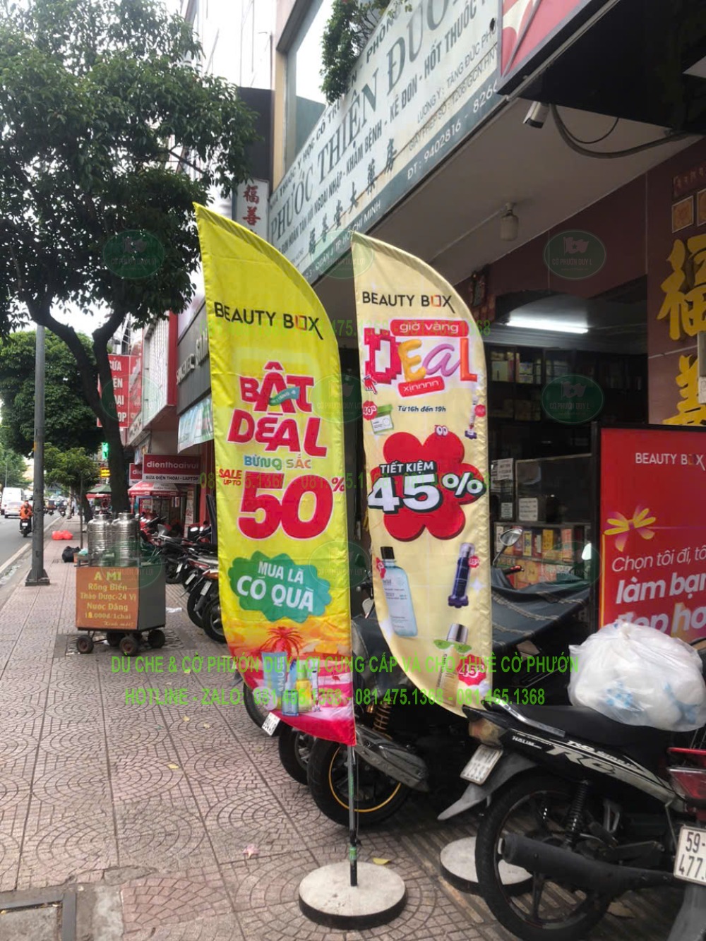 Hai cờ quảng cáo màu vàng mang nhận diện Beauty Box và thông điệp giảm giá, đặt trên đế tròn trước cửa hàng.