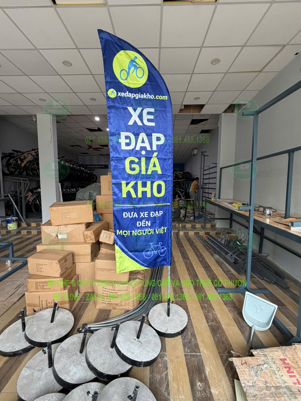 Cờ xanh và vàng mang tên “Xe đạp giá kho” được dựng trong khu vực có thùng hàng và các đế cờ tập kết.