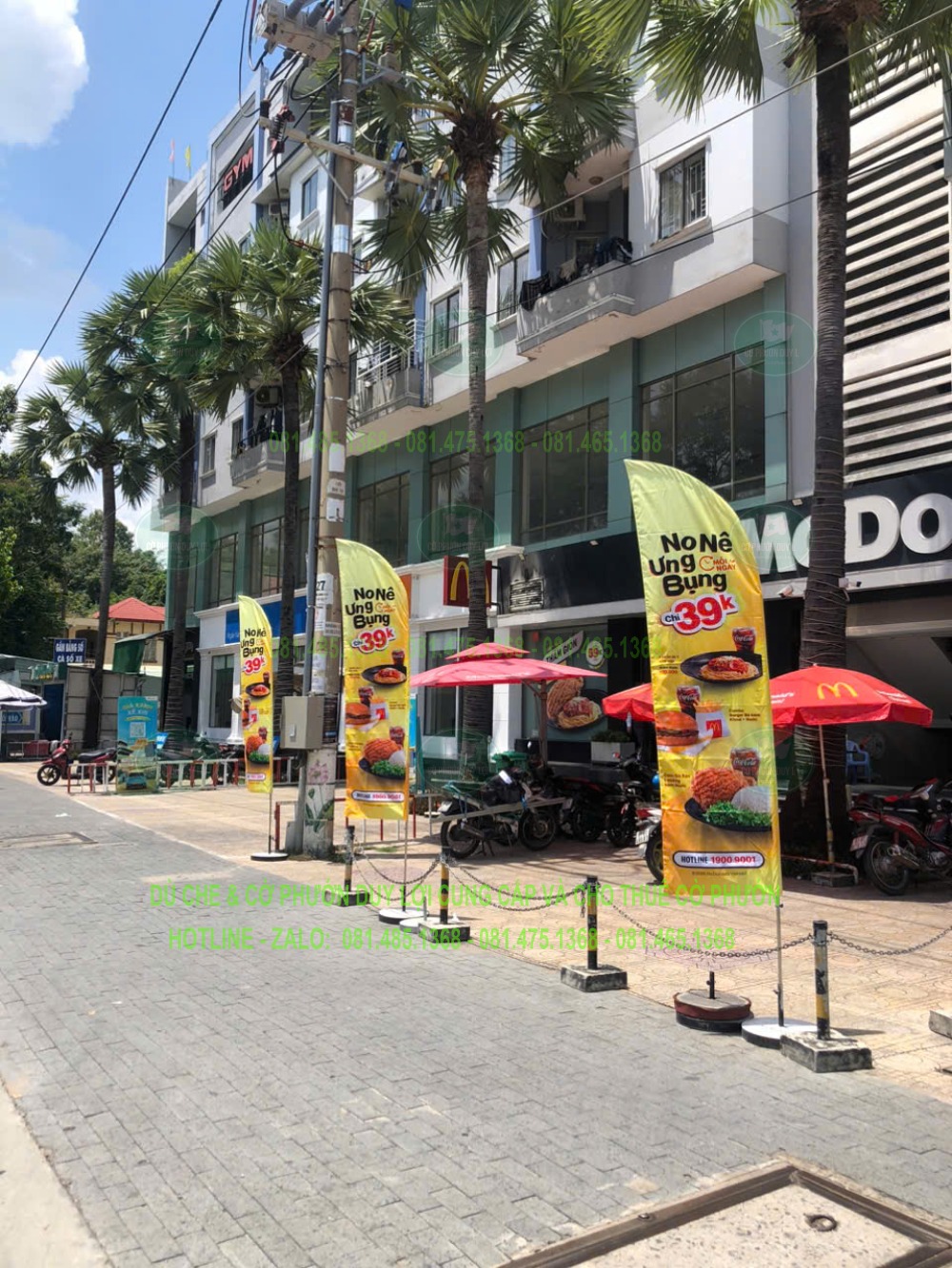 Nhiều cờ cánh buồm nền vàng được bố trí theo dãy trước cửa hàng McDonald’s, gần bảng hiệu và khu vực bàn ngoài trời.
