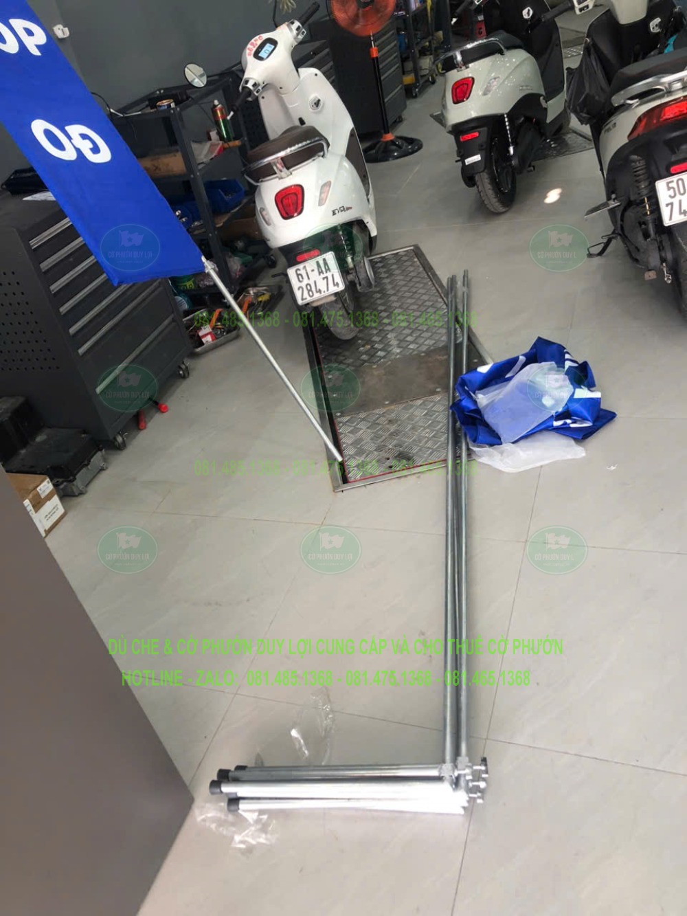 Các thanh khung kim loại và lá cờ màu xanh được đặt riêng tại cửa hàng xe, bên cạnh một bộ đang dựng.