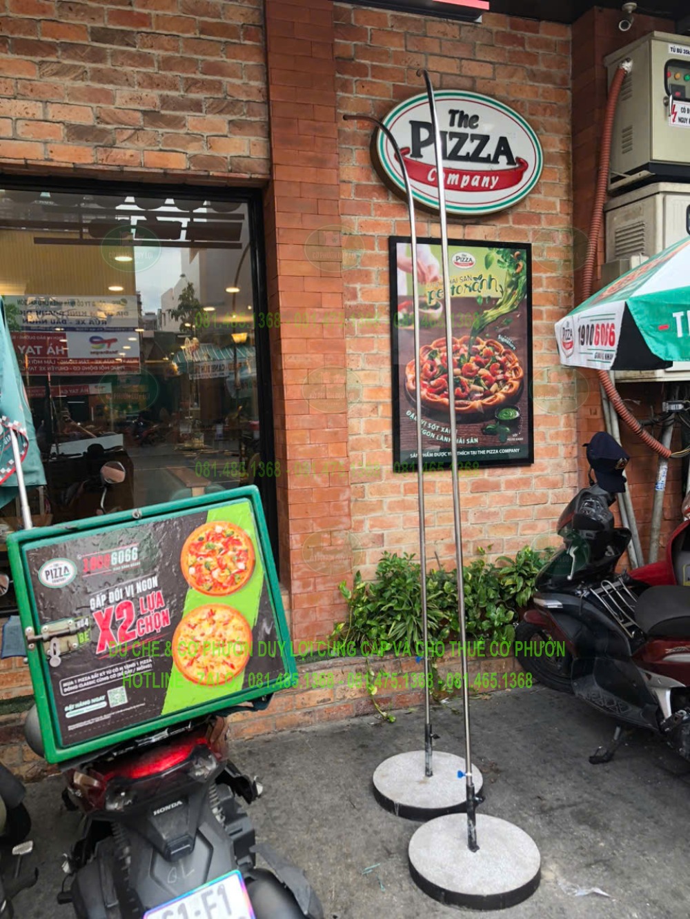 Hai khung đầu cong chưa lắp lá, gắn với đế tròn trước mặt tiền The Pizza Company.